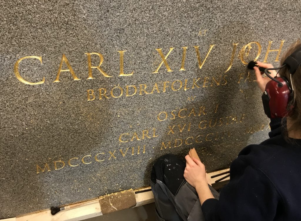 Stenhuggare arbetar med guldgravyr på granitmonument